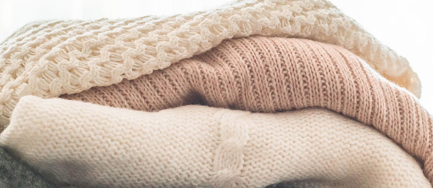 A stack of knitted sweaters in the interior of the living room. The concept of autumn winter comfort.