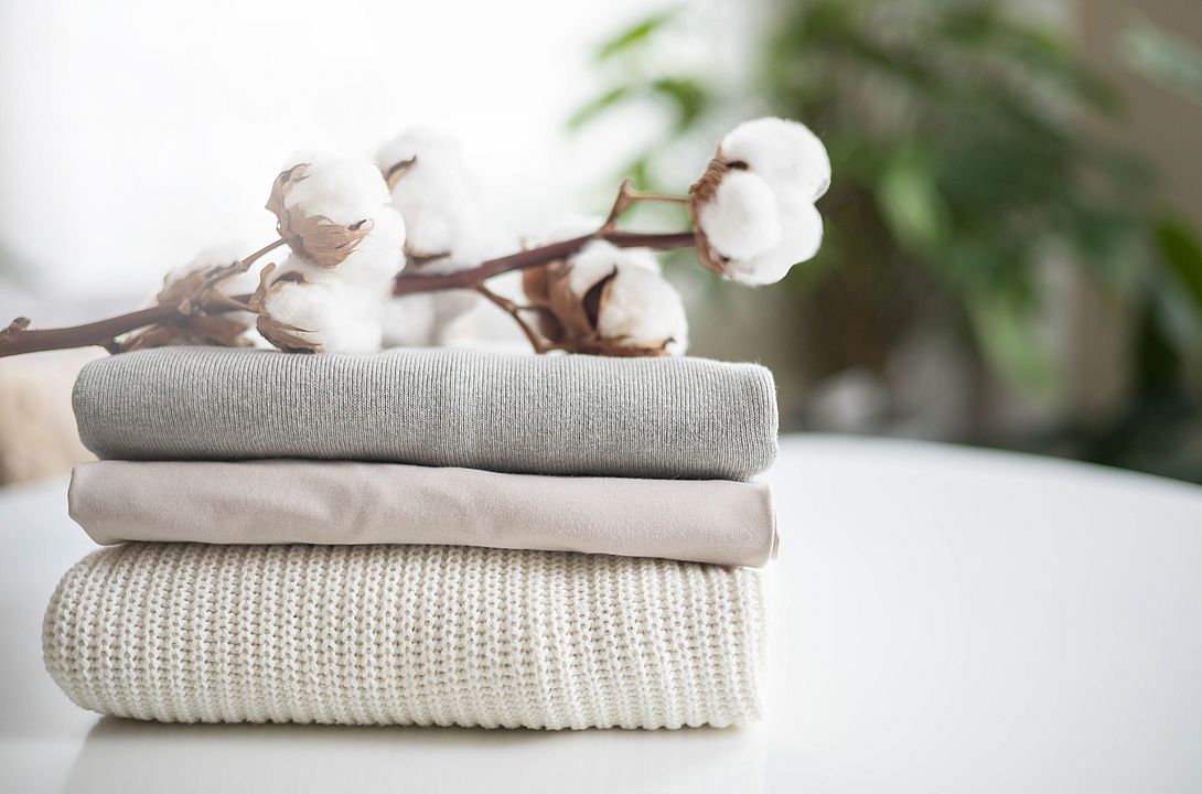 A neat stack of clean knitwear in neutral colors. Concept for sale, recycling and storage of clothing. Branch of cotton inflorescences.