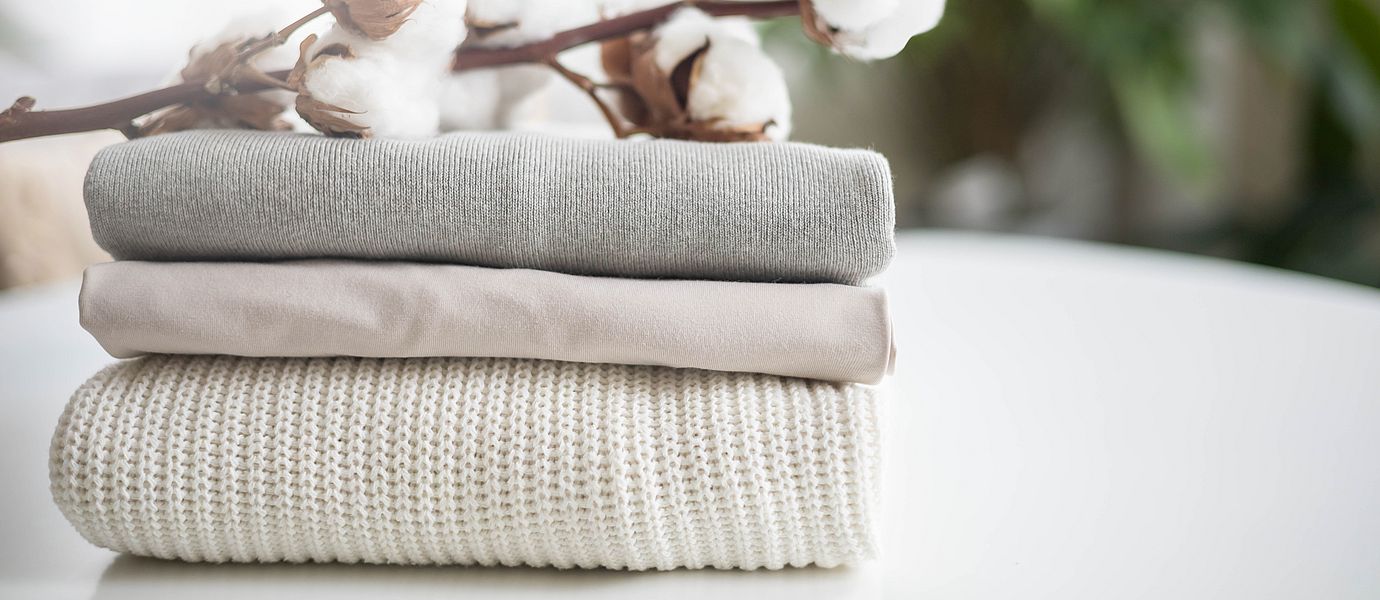 A neat stack of clean knitwear in neutral colors. Concept for sale, recycling and storage of clothing. Branch of cotton inflorescences.
